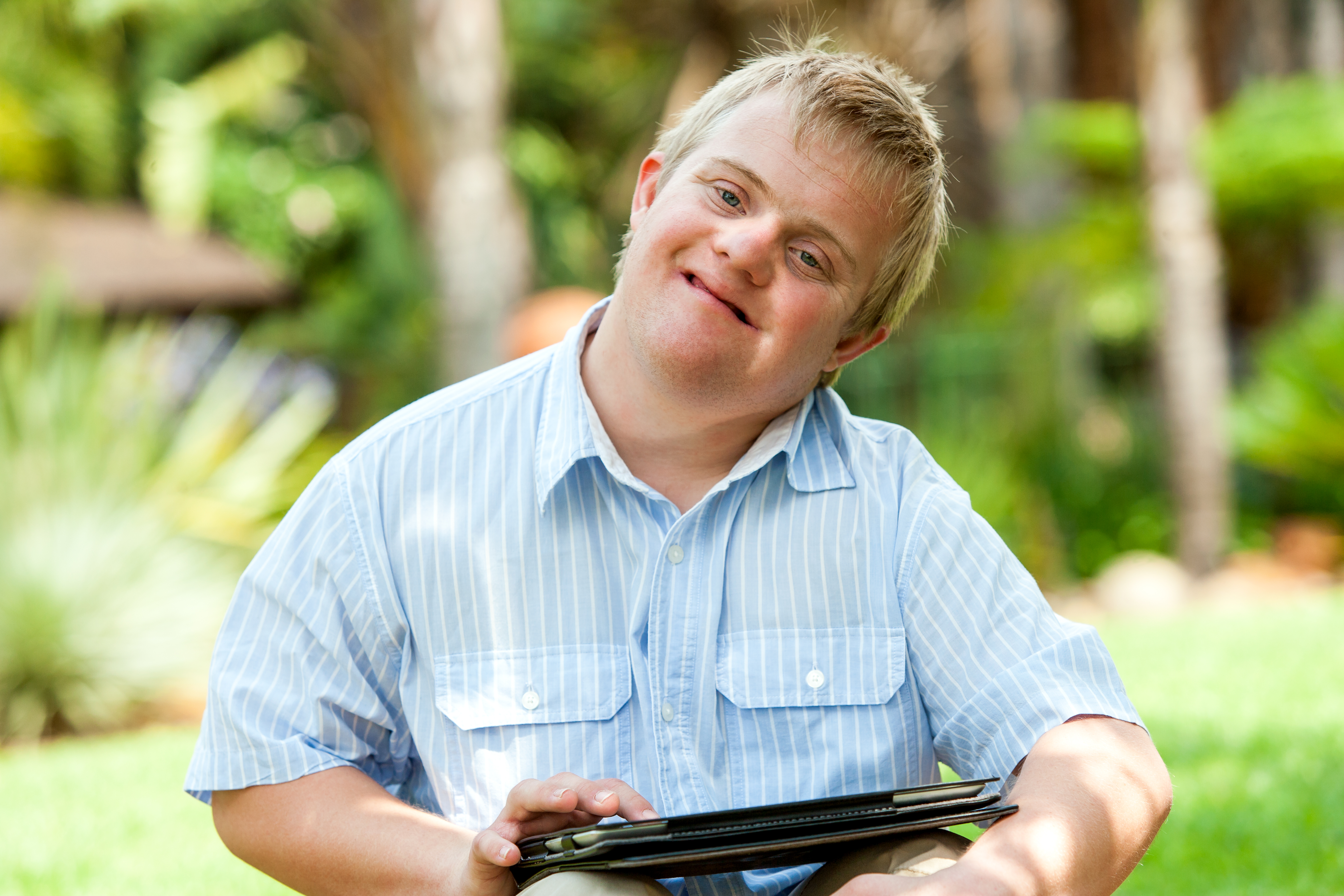 Close up portrait of handicapped boy playing on digital tablet outdoors.